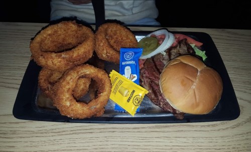 A plate with onion rings, a burger with lettuce and tomato, and condiments on the side.