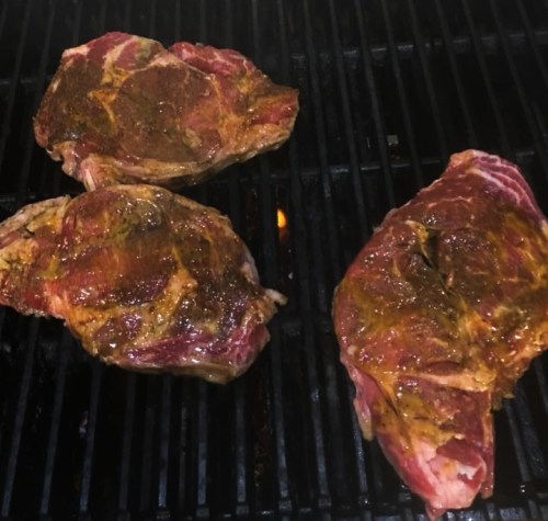 Three seasoned steaks grilling on a barbecue, with visible grill marks and a hint of smoke.