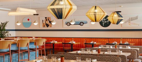 Brightly lit restaurant interior with colorful pendant lights, patterned seating, and modern artwork on the walls.