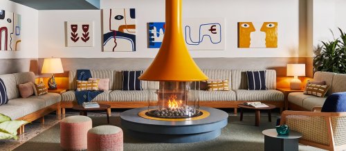 Cozy lounge with a central orange fireplace, modern art on the walls, and comfortable seating arrangements.