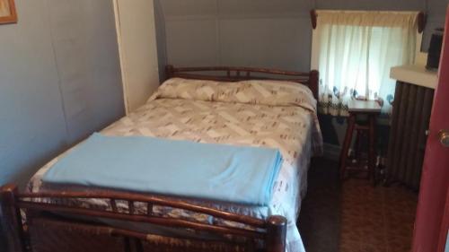 Cozy bedroom with a double bed, light blue blanket, and a small window with sheer curtains.