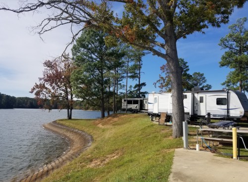 A serene lakeside scene with a camper, trees, and a clear blue sky, perfect for outdoor relaxation.