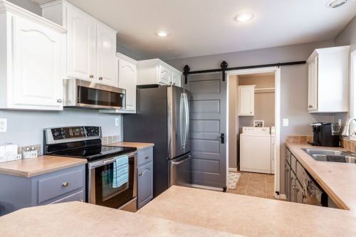 Modern kitchen with white cabinets, stainless steel appliances, and a sliding door leading to a laundry area.