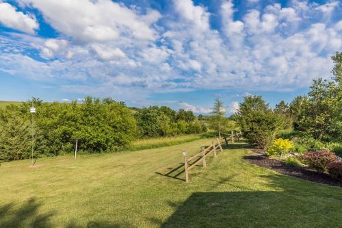 A lush green landscape with trees, a wooden fence, and a blue sky filled with fluffy clouds.