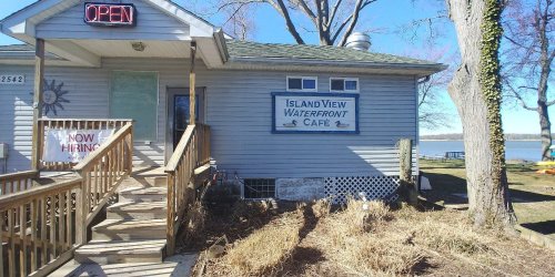 A waterfront café with a sign reading "Island View Waterfront Café," featuring a wooden ramp and an "Open" sign.