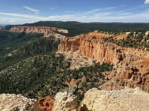 A panoramic view of rugged orange cliffs and green forests under a clear blue sky in a mountainous landscape.
