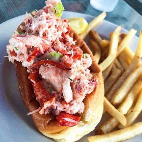 A lobster roll filled with lobster meat and vegetables, served with a side of crispy French fries.