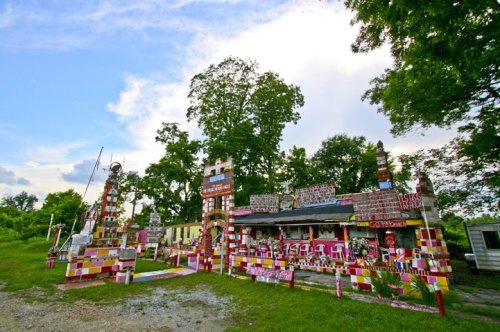Colorful, whimsical outdoor structure with various painted patterns and sculptures, surrounded by greenery and blue sky.