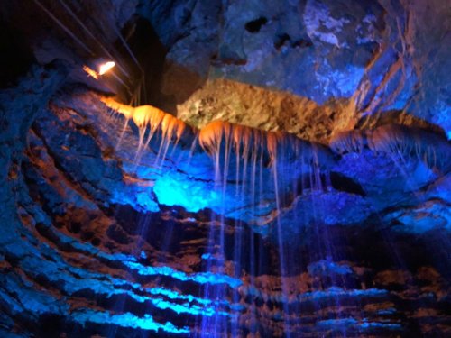 A cave interior with illuminated rock formations and water dripping down, creating a mystical blue ambiance.