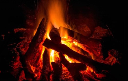 A glowing campfire with bright flames and burning logs against a dark background.