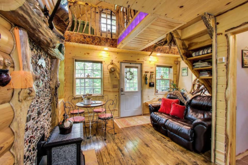 Cozy log cabin interior with wooden walls, a seating area, dining table, and staircase leading to a loft.