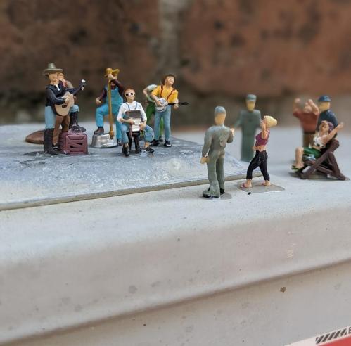 A group of miniature figures performing music and relaxing outdoors on a small stage.
