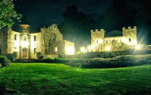 A stone castle illuminated at night, surrounded by lush green grass and a small pond.