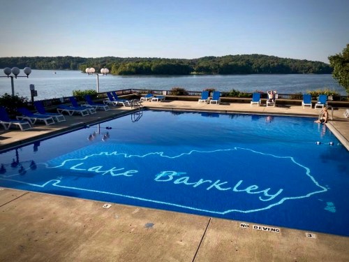 A swimming pool with "Lake Barkley" outlined on the bottom, surrounded by lounge chairs and a scenic lake view.