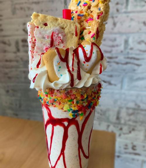 A colorful milkshake topped with whipped cream, sprinkles, a cookie, and drizzled with syrup.