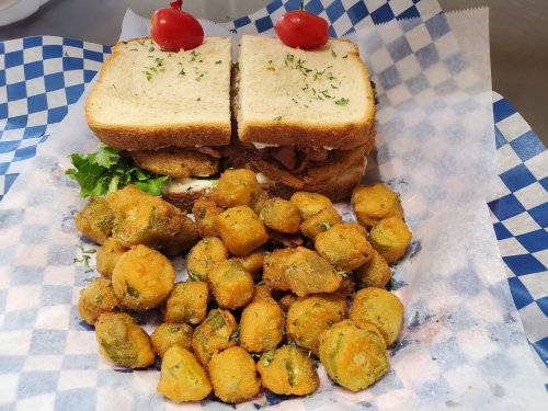 A sandwich with lettuce and cherry tomatoes, served with a side of fried okra on a blue checkered paper.