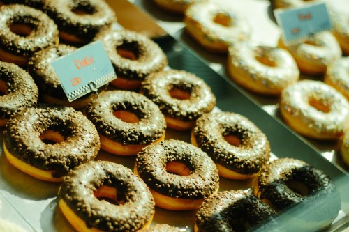 A display of assorted donuts, featuring chocolate and glazed varieties, topped with sprinkles and nuts.