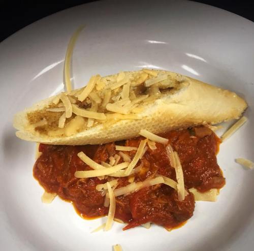 A plate featuring a stuffed bread roll topped with cheese, served with a rich tomato sauce underneath.