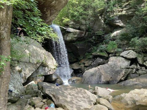 A serene waterfall cascades into a rocky pool surrounded by lush greenery and large boulders.