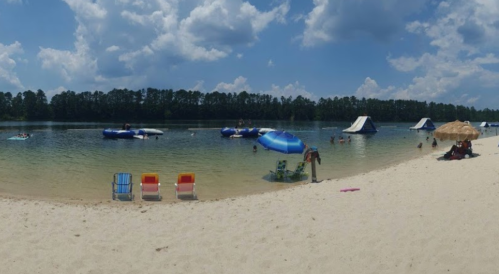 A sunny beach scene with people enjoying water activities, inflatable structures, and colorful beach chairs on the sand.