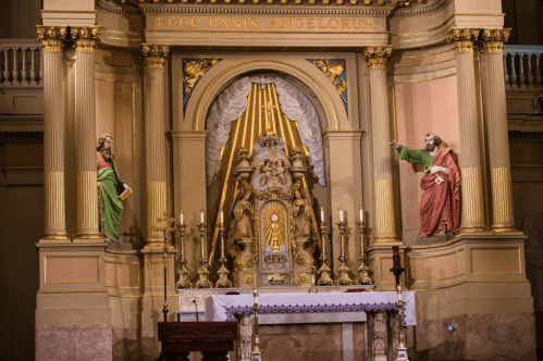 Altar with ornate decorations, featuring statues of saints and a central tabernacle in a church setting.