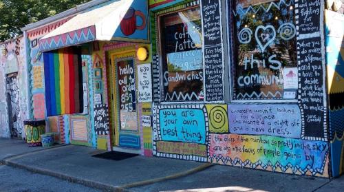 Colorful café exterior with vibrant murals, featuring messages of empowerment and community. Brightly painted door and windows.