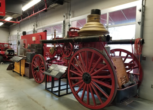 A vintage fire engine with large wooden wheels, displayed indoors alongside informational plaques.