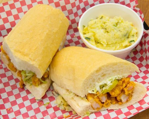 Two sandwiches filled with fried chicken and lettuce on a checkered paper, accompanied by a side of mashed potatoes.