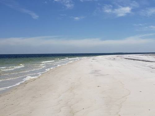 A serene beach with soft white sand, gentle waves, and a clear blue sky stretching into the horizon.