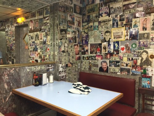 A cozy diner with a blue table, red seating, and walls covered in photos and dollar bills.