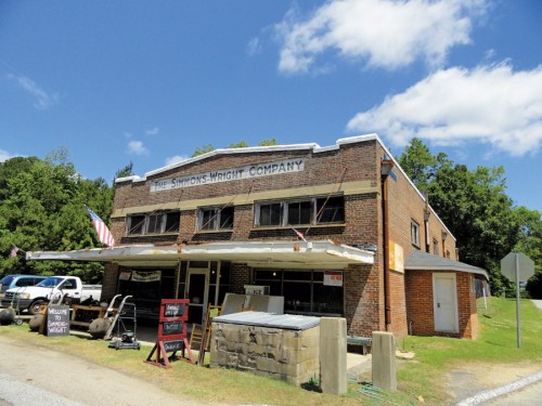 Historic brick building with "The Simmons-Wright Company" sign, surrounded by trees and a clear blue sky.