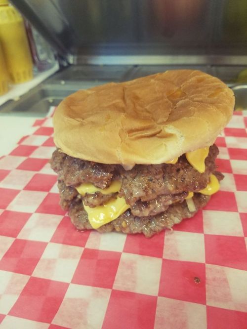 A towering double cheeseburger with melted cheese, stacked beef patties, and a soft bun on a red and white checkered paper.