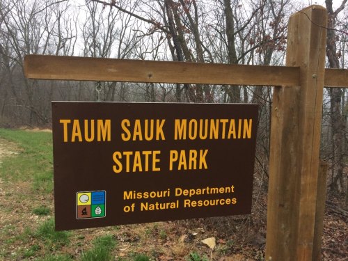Sign for Taum Sauk Mountain State Park, Missouri, surrounded by trees and grassy area.