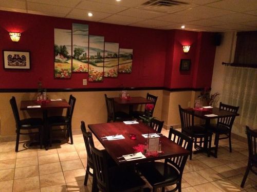 Cozy restaurant interior with wooden tables, chairs, and red walls adorned with artwork and soft lighting.