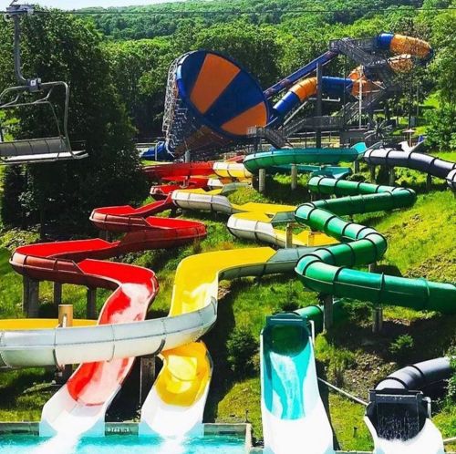 A vibrant water park featuring multiple colorful water slides winding down a green hillside.
