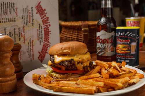 A juicy cheeseburger with lettuce and tomato, served with fries and drinks on a table with a menu in the background.