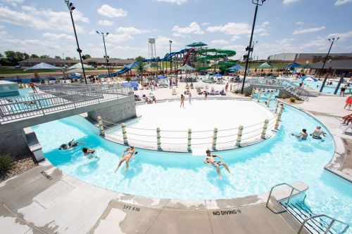 A sunny water park scene with a lazy river, water slides, and people enjoying the pool area.