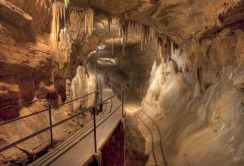 A dimly lit cave with stalactites and stalagmites, featuring a walkway for visitors.
