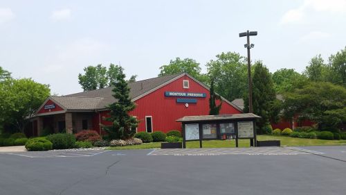 Red building with a sign reading "Montour Preserve," surrounded by greenery and a paved parking area.