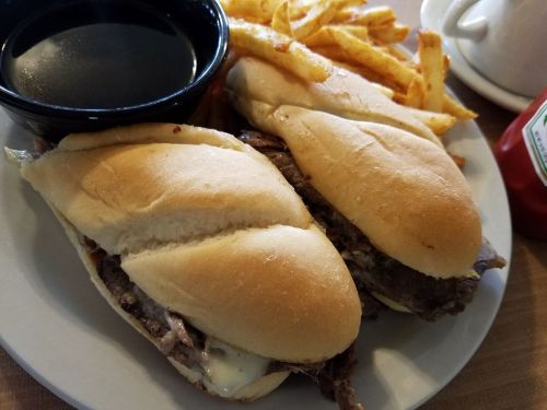 Two sandwiches filled with beef on a plate, accompanied by a side of fries and a small bowl of dipping sauce.