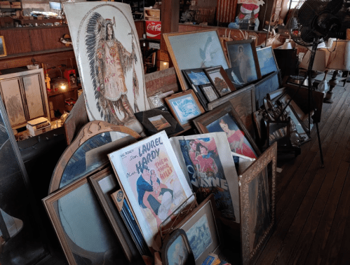 A collection of vintage framed artwork and photographs displayed on a wooden surface in a rustic setting.