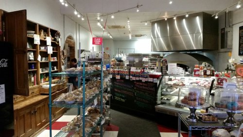 A cozy bakery interior with shelves of baked goods, a display case, and a counter for placing orders.