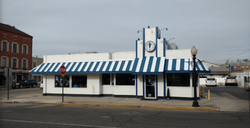 A white building with blue and white striped awning, featuring a clock tower, located on a street corner.
