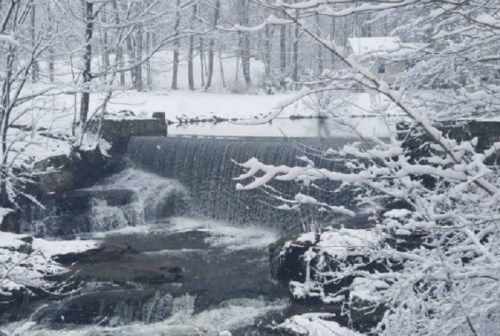 A serene winter scene featuring a snowy landscape with a waterfall and trees, creating a peaceful, tranquil atmosphere.