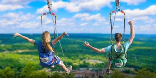 Two people ziplining over a lush green landscape, arms outstretched, enjoying the thrill of the ride.