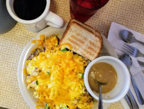 A plate of cheesy omelette with toast, a bowl of gravy, a cup of coffee, and a glass of red drink on a table.