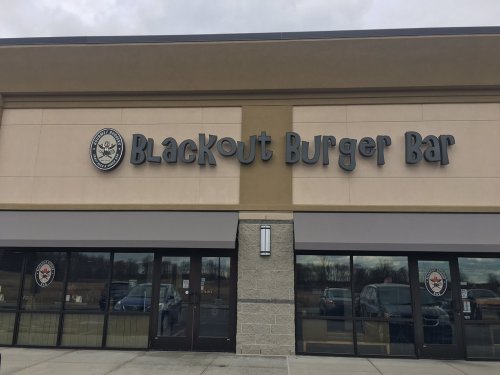 Exterior of Blackout Burger Bar, featuring a large sign and glass entrance, set against a cloudy sky.
