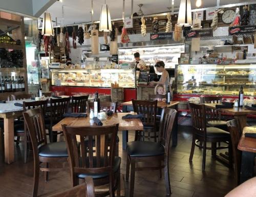 A cozy restaurant interior with wooden tables, chairs, and a display case filled with food in the background.