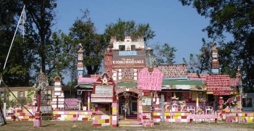 A colorful, whimsical building adorned with various signs and decorations, surrounded by trees and a clear blue sky.