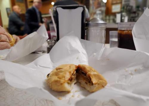 A partially eaten sandwich on a table, surrounded by crumpled paper and drinks in a diner setting.